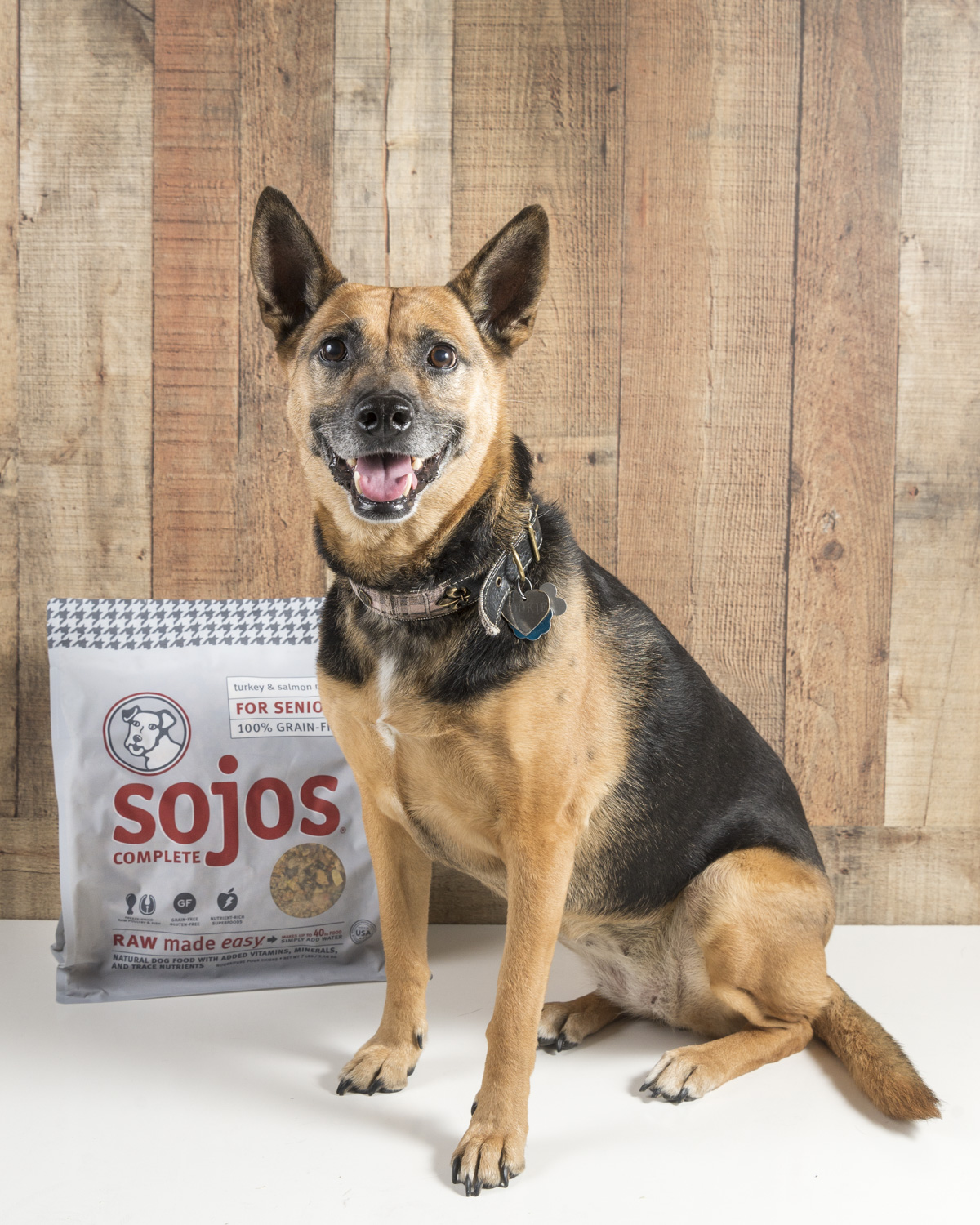 Sookie smiling beside a bag of original Sojos Complete senior dog food